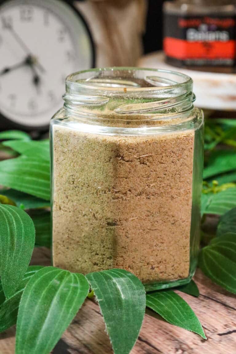 Delmas seasoning in glass jar wihtout a lid on top of greenery with a clock and another seasoning jar in the background.