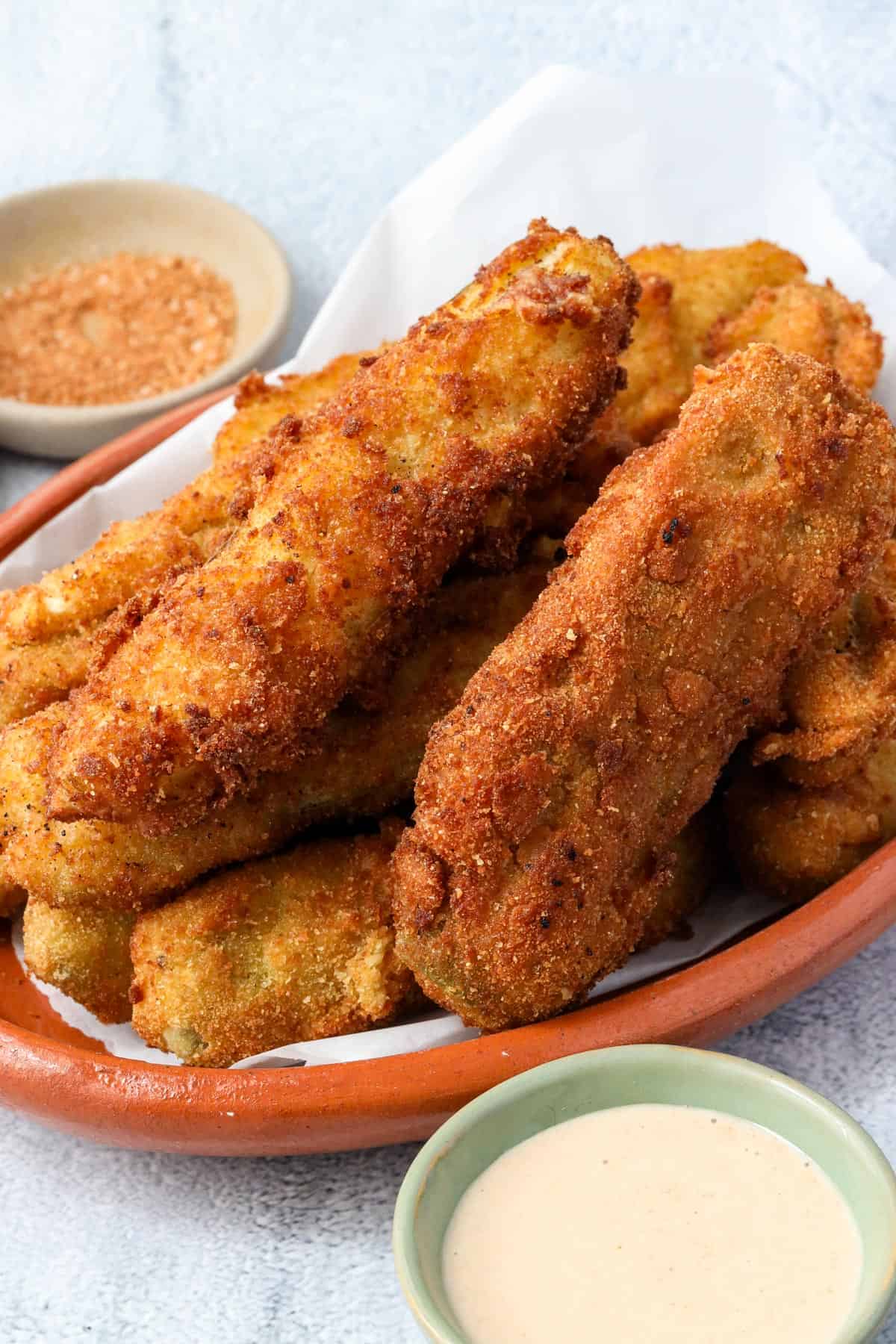 fried pickle spears layered on top of each other on a brown plate with dipping sauce in the background