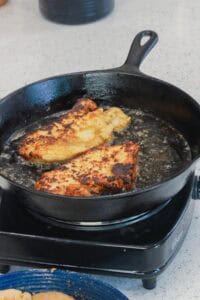 chicken breasts frying in cast iron skillet