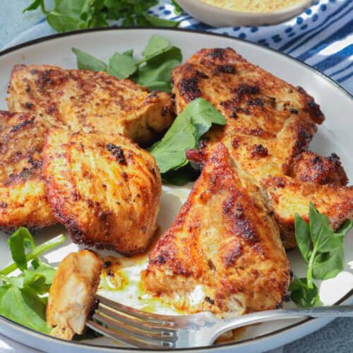 Fried chicken breast on white plate topped with herbs