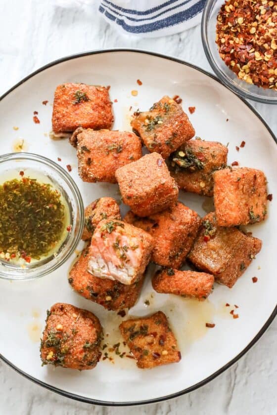 fried salmon bites with lemon-oil sauce on white plate