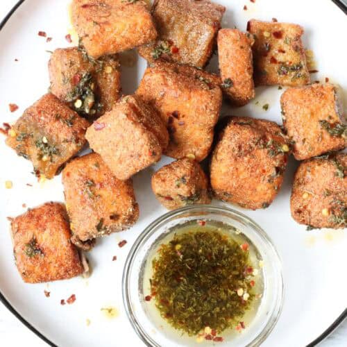 fried salmon bites with lemon-oil sauce on white plate