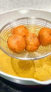 Fried potato balls on slotted spoon