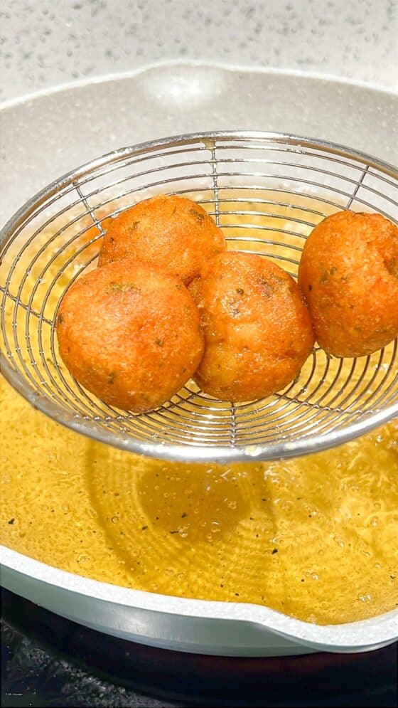 Fried potato balls on slotted spoon