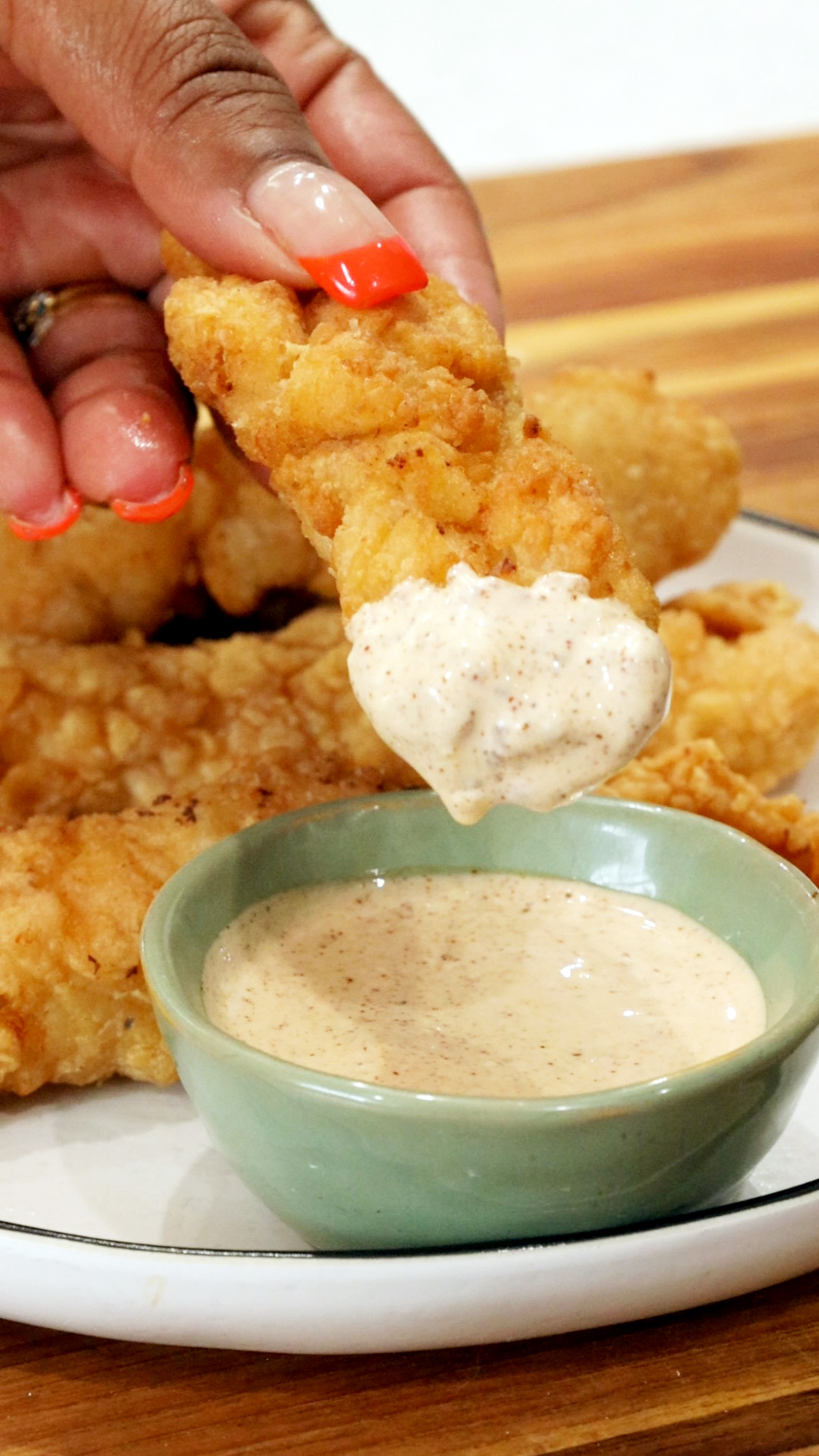 Fingers holding dipped chicken tenders above creamy sauce for chicken