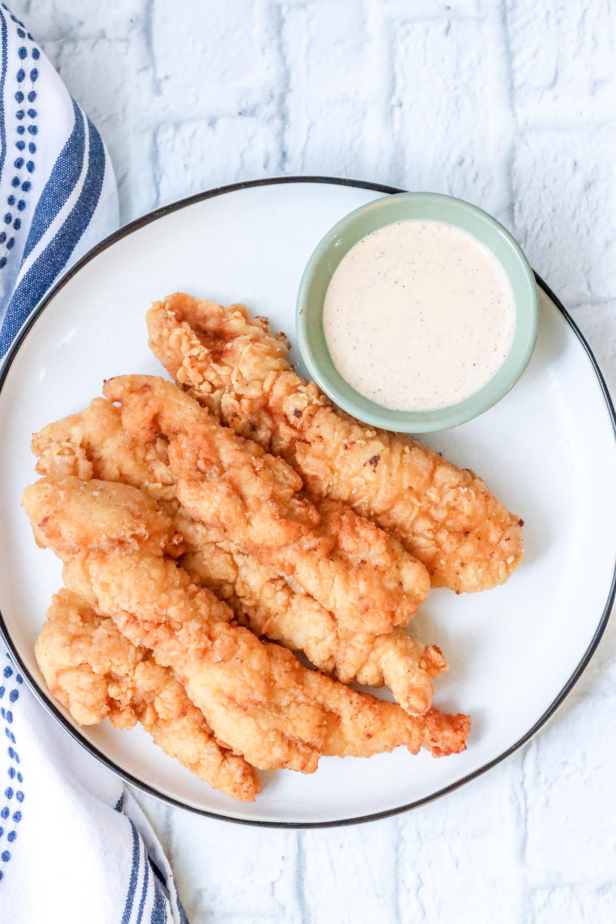crispy, golden, and juicy fried chicken tenders on white plate with dipping sauce.