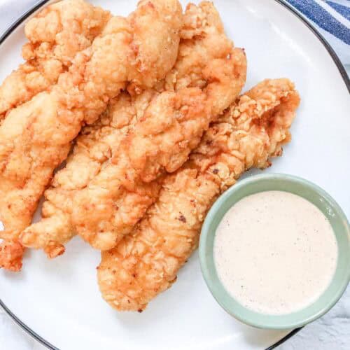 crispy, golden, and juicy fried chicken tenders on white plate with dipping sauce.