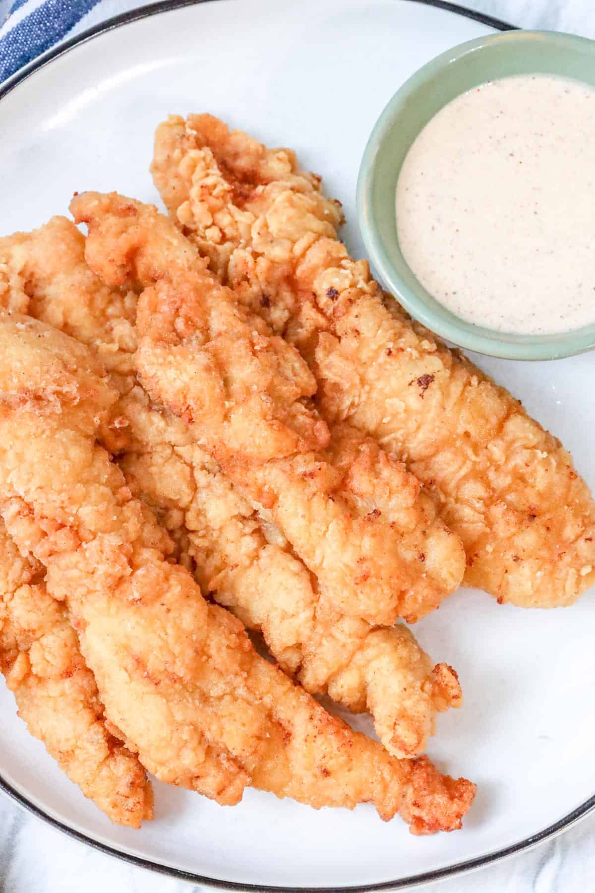 crispy, golden, and juicy fried chicken tenders on white plate with dipping sauce.