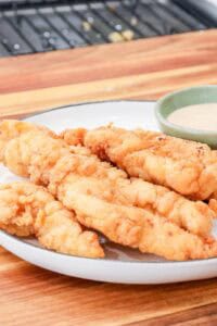 crispy, golden, and juicy fried chicken tenders on white plate with dipping sauce.