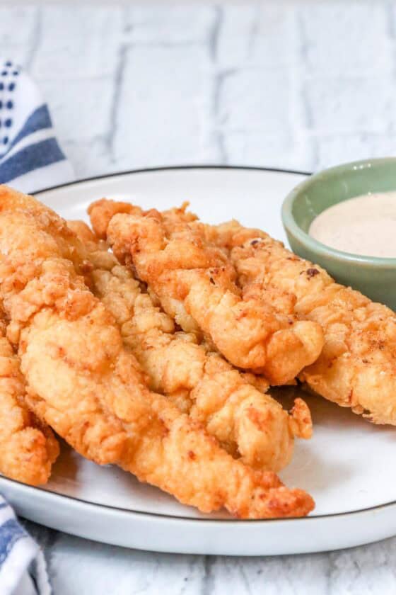 crispy, golden, and juicy fried chicken tenders on white plate with dipping sauce.