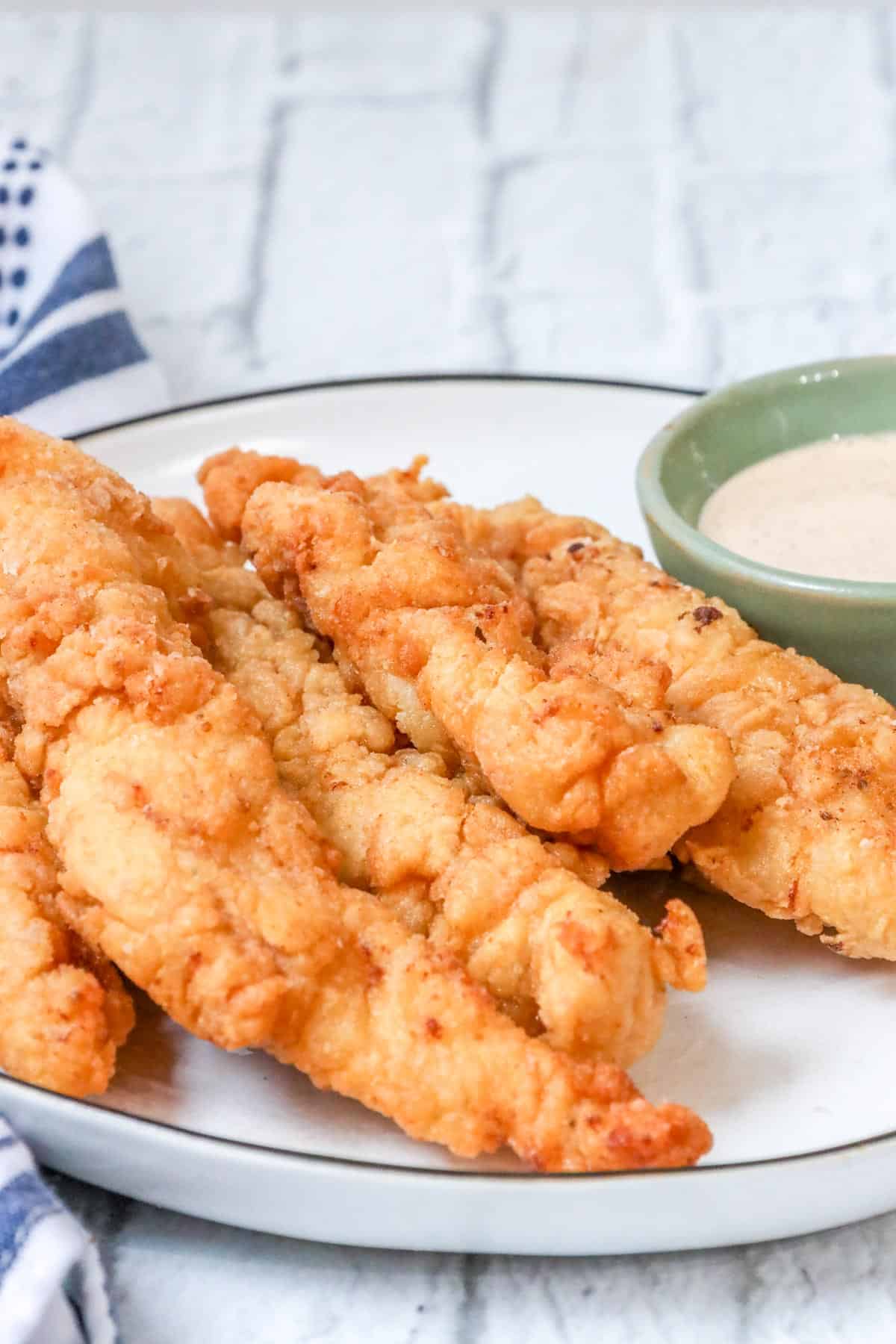crispy, golden, and juicy fried chicken tenders on white plate with dipping sauce.