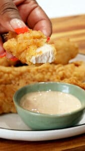 hand holding chicken fingers over dipping creamy sauce for chicken