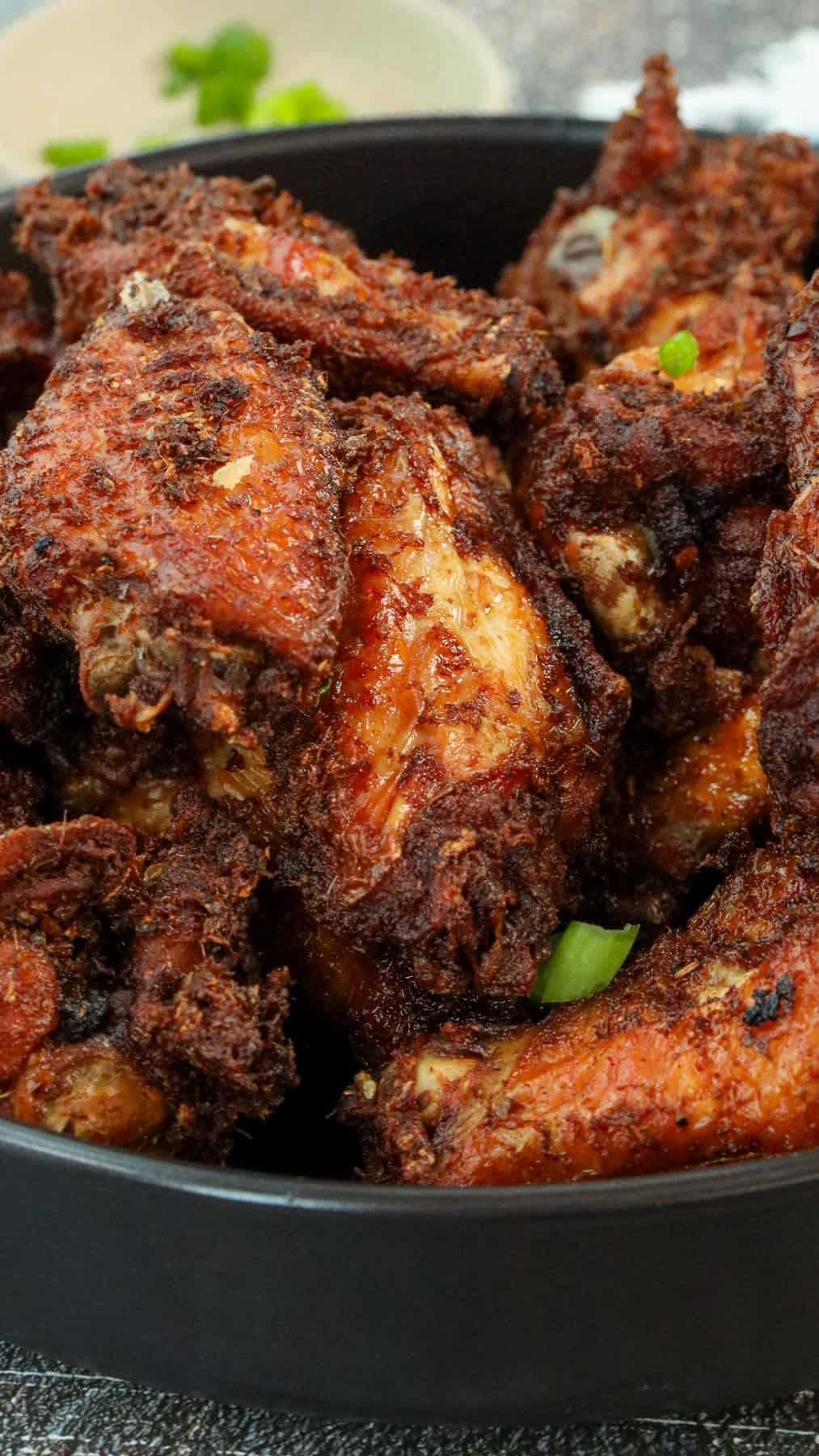 Fried Soy Sauce Garlic Chicken Wings topped on each other in black bowl topped with green onions