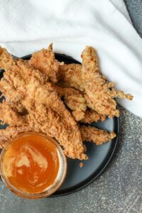 Southern Fried Chicken strips with sauce on black plate