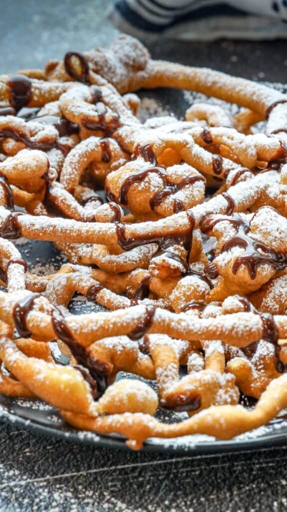 funnel cake made at home dusted with powdered sugar and drizzled with chocolate