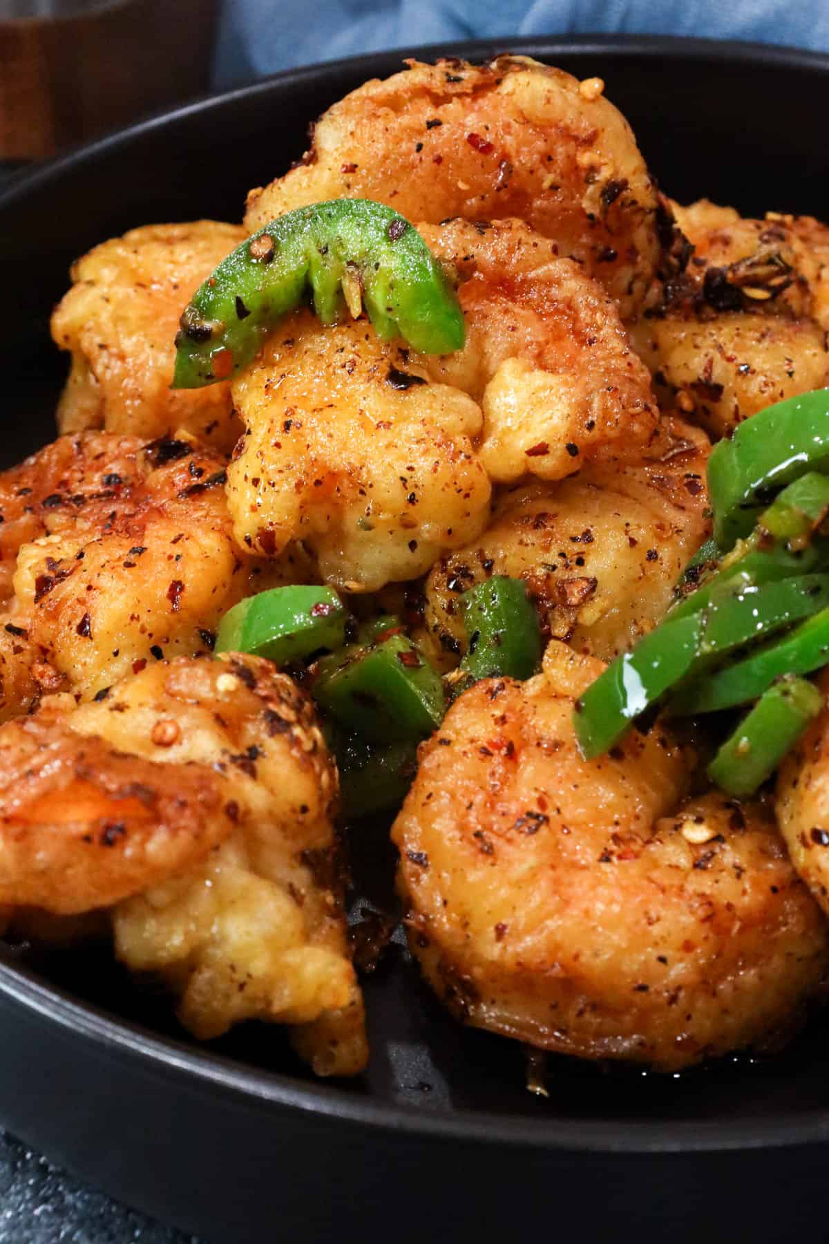 fried salt and pepper shrimp in large black bowl topped with chili peppers