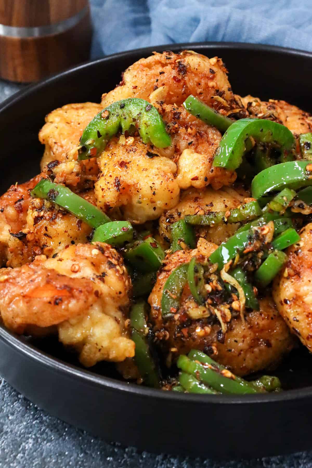 fried salt and pepper shrimp in large black bowl topped with chili peppers