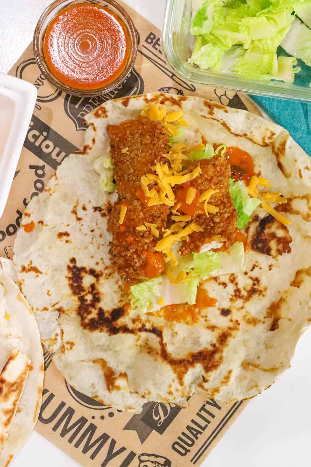 crispy Korean inspired chicken wrap topped with cheese and Gochujang sauce