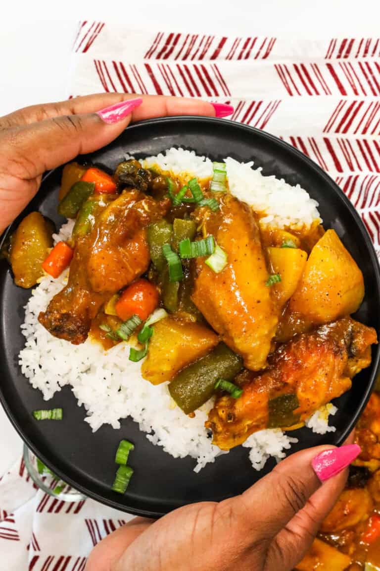 hands holding a plate of rice topped with air fryer curry chicken