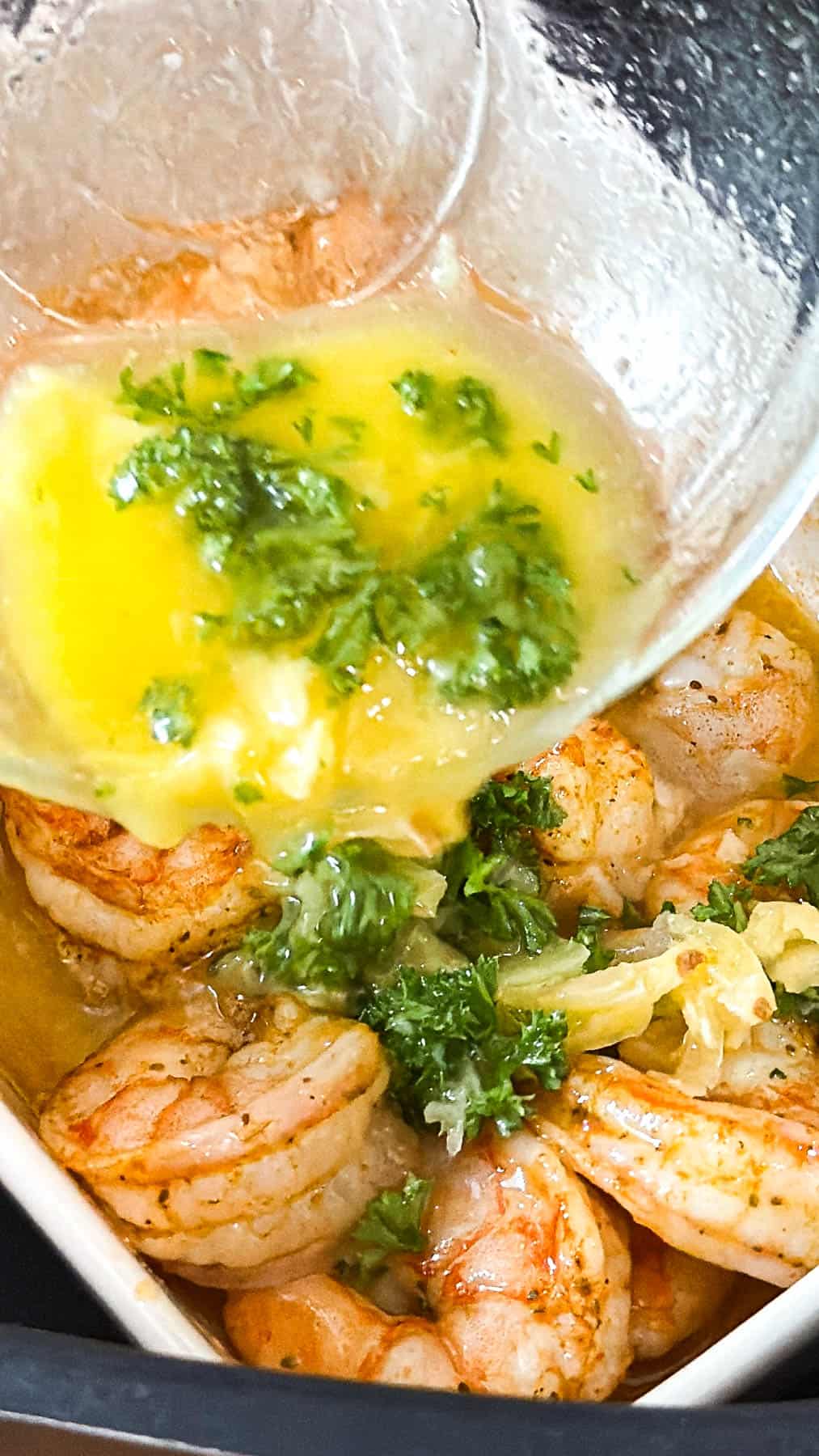 pouring garlic butter with parsley over air fryer shrimp