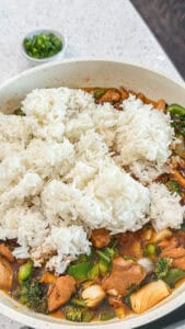 Cooked white rice added to seasoned chicken and vegetables in a skillet for homemade gochujang fried rice.