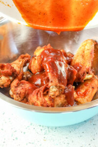 pouring bbq sauce over fried wings